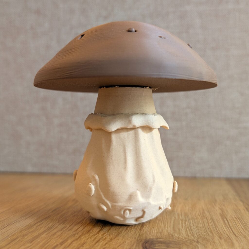 Gedruckter Deko-Pilz mit braunem Hut und knochenfarbenem Stiel, frontal auf einer Holzplatte
